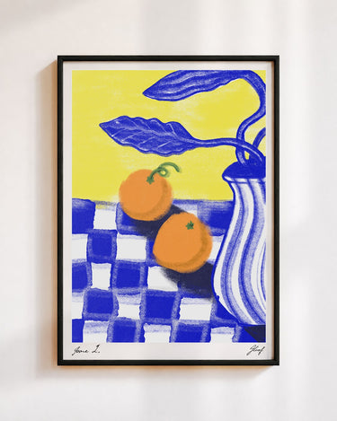 Two Oranges poster in a black frame on a white wall: two oranges on a blue and white checked cloth beside a striped blue vase