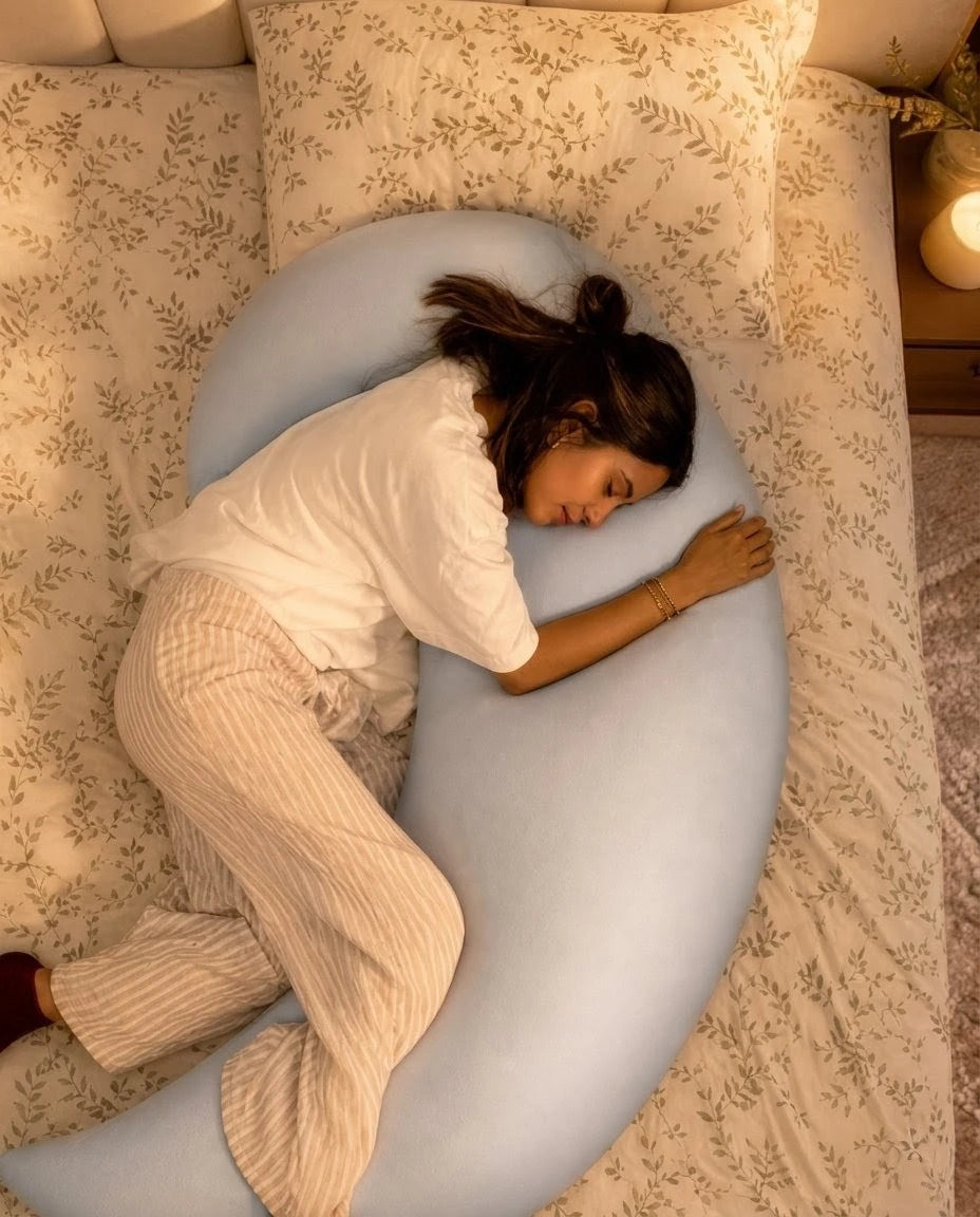 Woman lying on a large moon shaped pillow in a cozy bedroom setting.