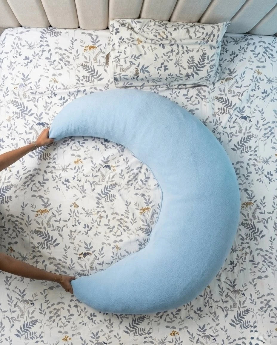 Blue crescent-shaped pillow on a bed with floral bedding