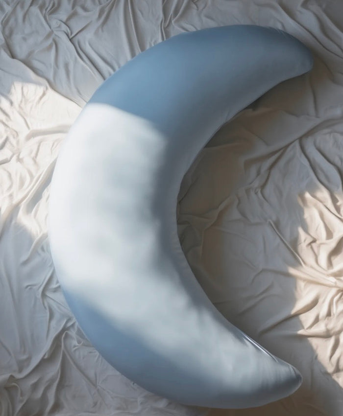 Floof Body Pillow in baby blue, a crescent moon shape on white bedding