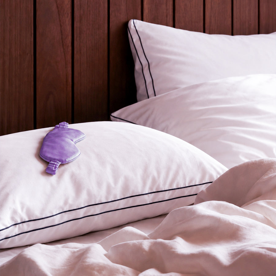 Two Floof Cloud Pillows on a made bed against a dark wood headboard, with a purple eye mask resting on one