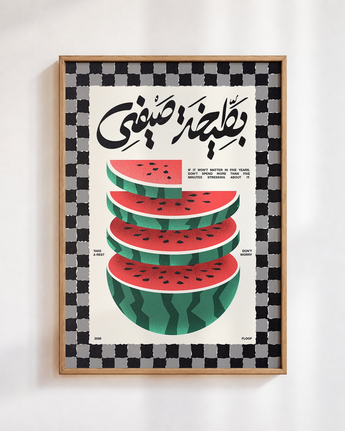 Bateekha poster in a wooden frame on a white wall: stacked slices of watermelon under the Arabic words بطيخة صيفي, inside a black and white checked border