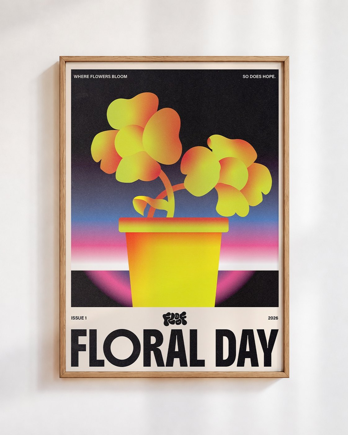 Floral Day poster in a wooden frame on a white wall: two yellow and orange flowers in a yellow pot against a pink and blue sunset, above the words Floral Day