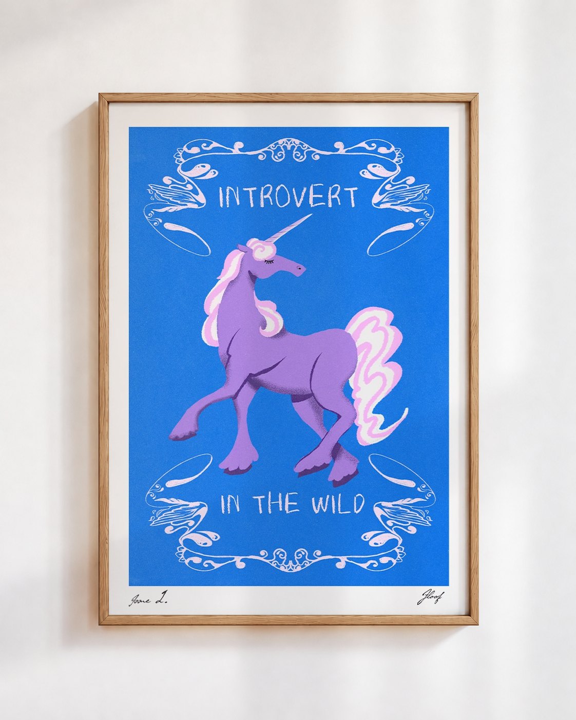 Introvert in the Wild poster in a wooden frame on a white wall: a lilac unicorn inside white swirls on cobalt blue, with the words Introvert in the Wild