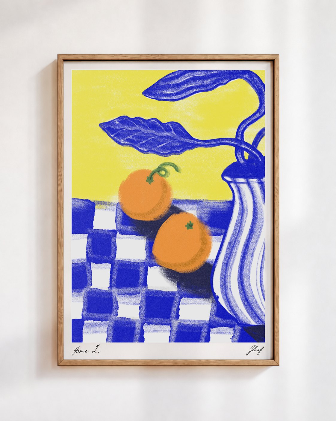 Two Oranges poster in a wooden frame on a white wall: two oranges on a blue and white checked cloth beside a striped blue vase